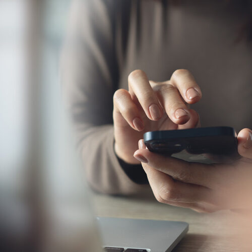 Close up, business woman using mobile phone with laptop computer on office table. Woman using smartphone for online shopping and digital banking via mobile app, social media marketing